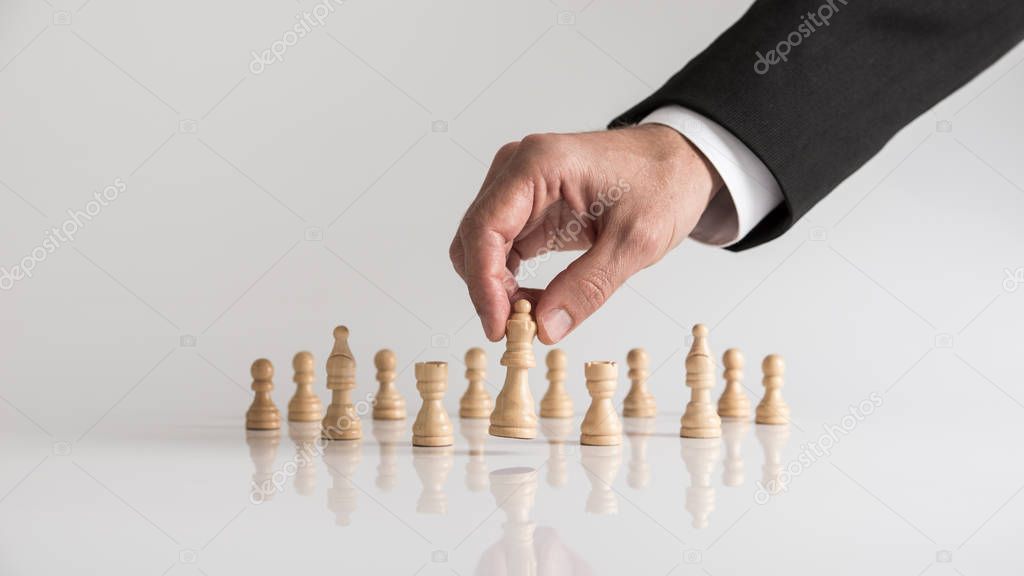 Man in business suit playing chess moving the queen piece lifting it up in his fingers. Conceptual of strategy planning.