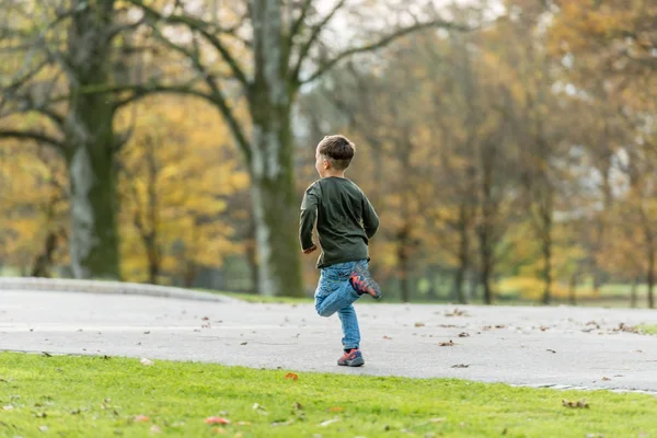 秋の公園の道で走っている若い少年の側背面図 — ストック写真