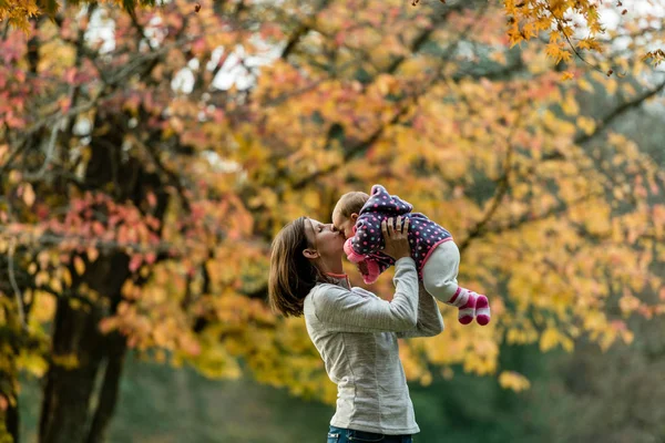 屋外の公園でカラフルな木で母キス若い赤ん坊少女の秋の風景 — ストック写真