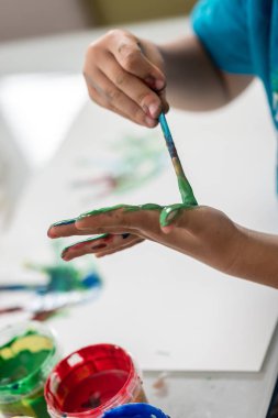 O onun hurma bir fırça ile renkler gibi eğlenceli renkli el ile olan bir çocuğun görünümünü Closeup boyalar.