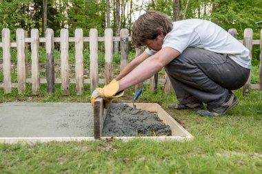 Genç adam ahşap tahta bir DIY kavram içinde yeni beton temel atma kullanarak bir arka bahçesinde çimento tesviye.