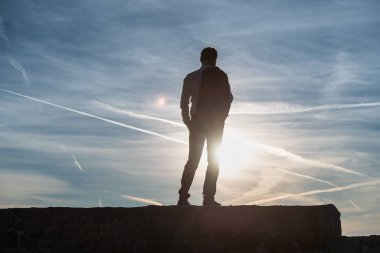 Manzarası batan güneşin contrails ve kopya alanı ile kontrast bir duvar üzerinde duran adam.