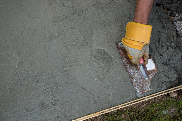 Closeup of gloved hand leveling fresh concrete floor outside in backyard.