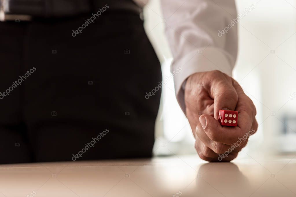 Businessman in suit throwing red dice over office table, business risk concept.