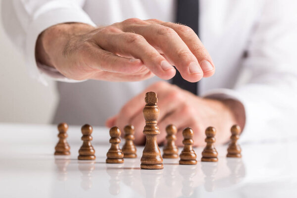Концепция лидерства в бизнесе - мужской жест защиты от деревянных шахматных фигур перед королем
.