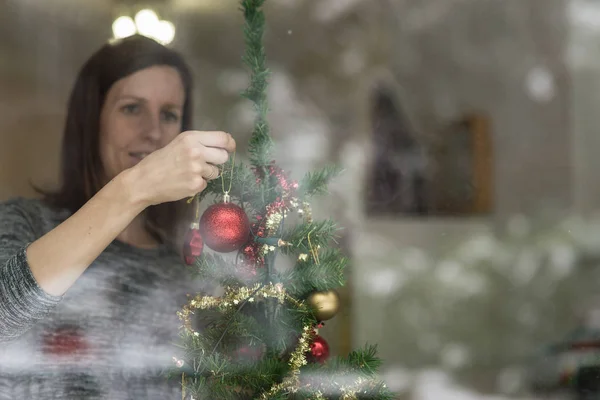 Sorrindo Jovem Mulher Decorando Árvore Natal Colocando Bola Vermelha Ramo — Fotografia de Stock