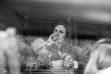 Gri tonlamalı görüntü düşünceli elinde eğilerek kafede tek başına oturan genç bir kadın.