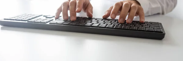 Wide view image of programmer using computer keyboard on white office desk.