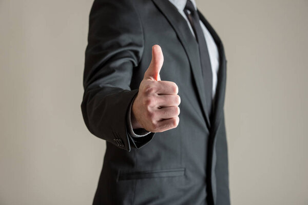 Front view of businessman showing a thumbs up sign over grey background.