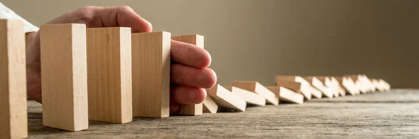 Closeup of businessman stopping collapsing dominos from falling with his hand. Wide view image.