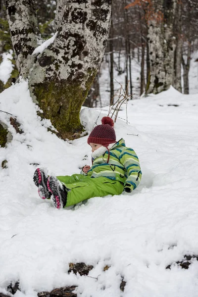 穿着绿色保暖冬装躺在雪地里的小男孩很开心 — 图库照片