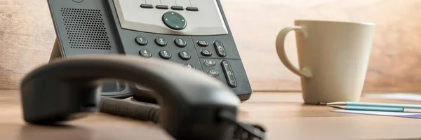 広視野黒固定電話の横にあるフックとコーヒーのマグカップをオフ携帯電話の木製オフィス デスク — ストック写真