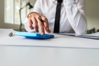 Mimar ya da bir proje üzerinde çalışırken bir hesap makinesini kullanarak onun ofis masasında oturan.