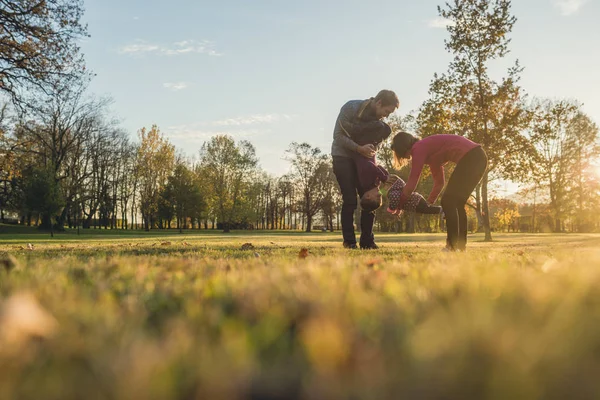 在阳光明媚的秋日 父母举起和孩子一起玩耍时 带着两个孩子在公园里玩得很开心的年轻家庭 — 图库照片