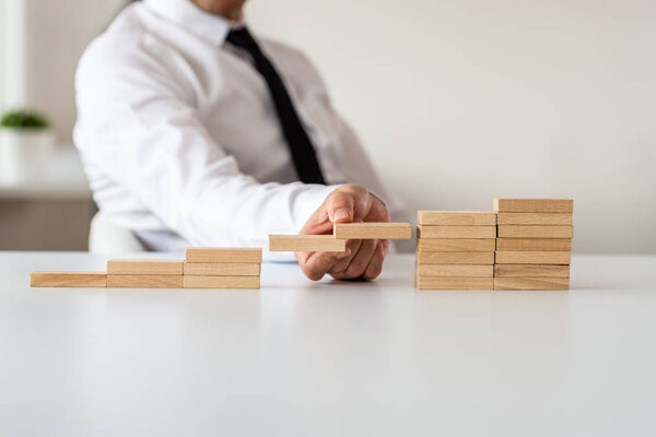 Business leader making plans for the future in a conceptual image as he supports two of the steps made of wooden pegs.