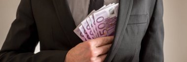 Geniş görüş görüntüsü 500 Euro faturaları takım elbise ceketinin iç cebine koyarak işadamı. Gri arka plan üzerinde.