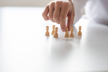 Köylü satranç taşları kavramsal bir görüntüde beyaz ofis masasında liderlik ve insan kaynakları düzenleme iş adamı el closeup.