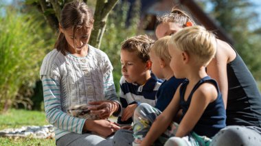 Çeşitli yaş ve anneleri dışında onların şirin evde beslenen hayvan adatavşanı sevişme bir çim üzerinde oturan dört çocuk.