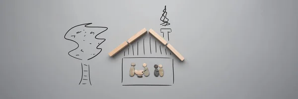 Family vision of a safe home in a conceptual image with family made of pebbles in a handdrawn house with wooden roof and a tree next to it.
