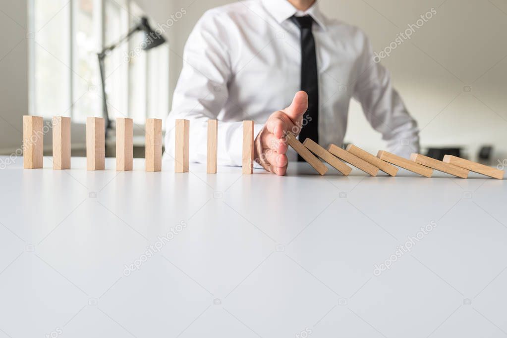 Businessman intervening to stop falling dominos with his hand in a conceptual image.