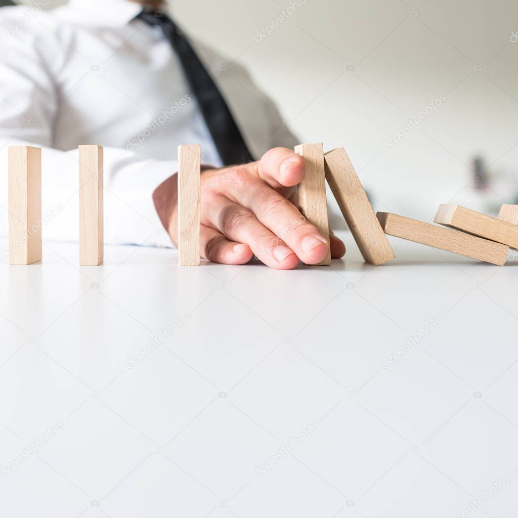Businessman placing his hand to stop falling dominos and prevent the crisis in a conceptual image.