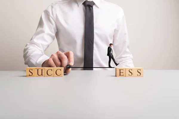 Businessman walking across a black marker line that connects wooden blocks to spell the word Success.