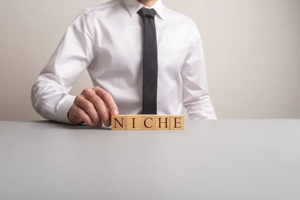 Empresário sentado em sua mesa de escritório montando uma palavra NICHE — Fotografia de Stock