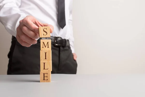 Empresário empilhando cubos de madeira para soletrar a palavra Sorriso — Fotografia de Stock
