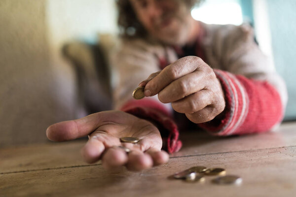 Low angle view of an old man in torn sweater counting Euro coins