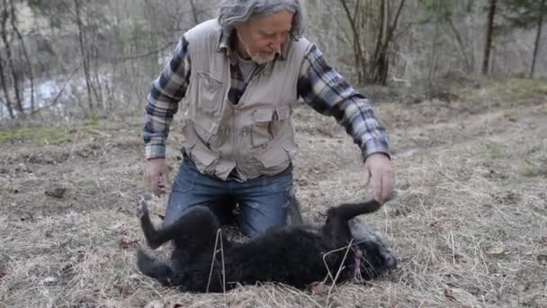 Homme âgé assis sur le sol près de la rivière jouant avec son chien noir — Video