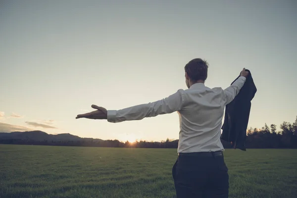 Empresário em pé no prado verde olhando para o pôr do sol — Fotografia de Stock