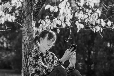 Bir ağacın altında oturan cep telefonu kullanan kadın