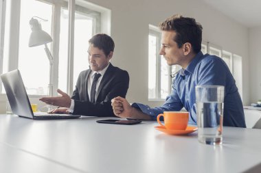 Ofis masasında oturan iki işadamı birlikte çalışıyor.