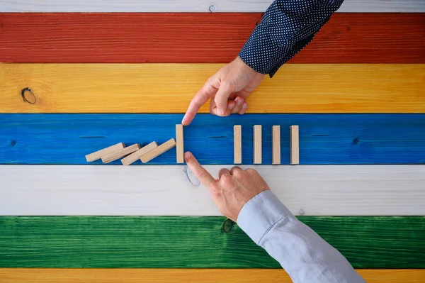 Zwei männliche Hände arbeiten zusammen, um Dominosteine vor dem Zusammenbruch zu bewahren — Stockfoto