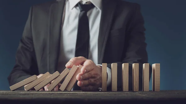 Business executive stopping collapsing dominos with his hand — Stock Photo, Image