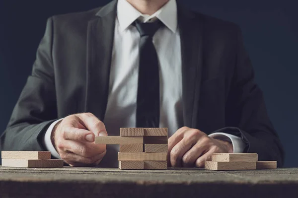 Front view of businessman at his desk making a stack of wooden p — Stock Photo, Image