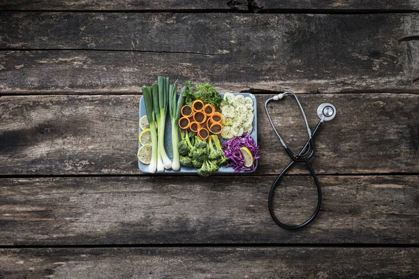 Healthy eating and diet - plate full of fresh vegetables next to a stethoscope placed on rustic wooden boards.