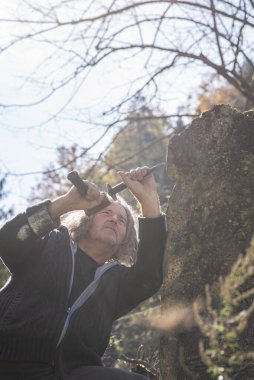 Kıdemli bir sanatçının çekiç ve keskiyle taş heykel yontması, güneş ışığının dışında çalışması..