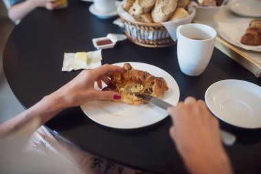 Kadın elleri tereyağı ve reçel sürerken enfes kruvasanın üzerine tam kahvaltı masasında.