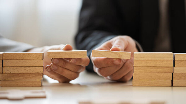 Closeup view of businessman and businesswoman making a bridge of wooden blocks between two stacks of them in a conceptual image of merger and cooperation.