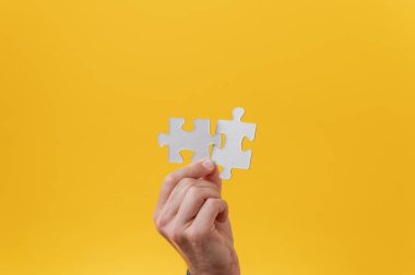 Erkek el kavramsal bir resimde elinde birbirine uyan iki yapboz parçası tutuyor. Sarı arkaplan.