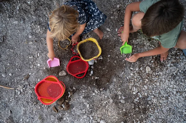Top view of brother and sister playing with pebbles, dirt and sand toys.