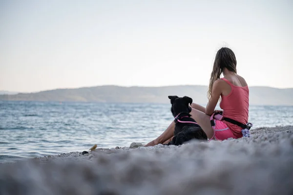 Mladá Žena Sedí Krásné Oblázkové Pláži Svým Černým Ovčáckým Psem — Stock fotografie