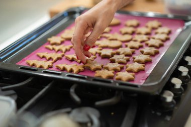 Kırmızı manikürlü kadın elinin düşük açılı görüntüsü. Bayram şeklinde zencefilli kurabiyeleri pişirme tepsisine koyuyor..