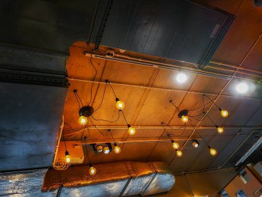 Havalandırma boruları ve dekoratif turuncu ampulleri olan tavan.