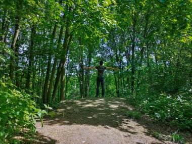 Tepenin kenarındaki ince ağaçlı tişörtlü adam.