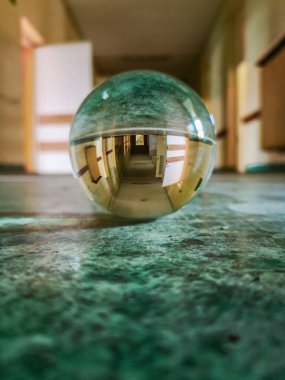 Long corridor with green covering on the floor reflected in crystal glassy lensball in old abandoned hospital clipart