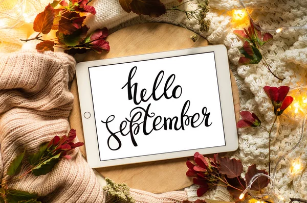 The tablet says the word hello September with red leaves and a dais on the wooden background. Concept of the autumn. View from above. — Stock Photo, Image