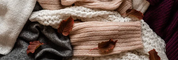 Background with warm sweaters. Pile of knitted clothes with autumn leaves, warm background, knitwear, space for text, Autumn winter concept. Copy Space.