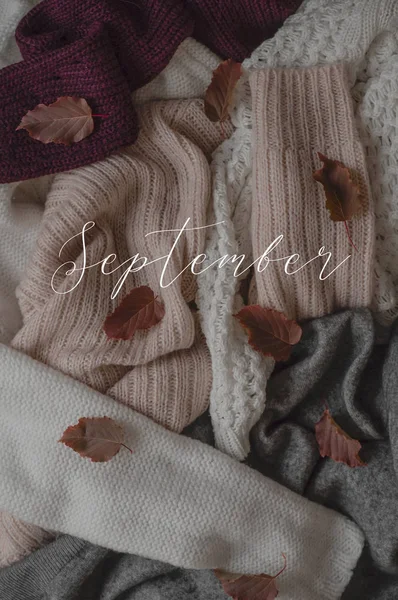 Bakgrund med varma tröjor och inskriptionen September. Högen av stickade kläder med höst löv, varm bakgrund, stickat, hösten koncept. — Stockfoto